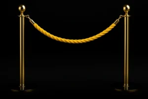 Luxury gold stanchions with a velvet yellow rope against a black background, symbolizing exclusive VIP real estate service with Ivan Larco in Orange County.