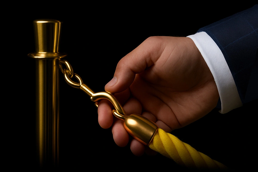Close-up of a hand in a blue suit unhooking a luxury gold stanchion with a yellow velvet rope, symbolizing exclusive access to premium real estate services with Ivan Larco.
